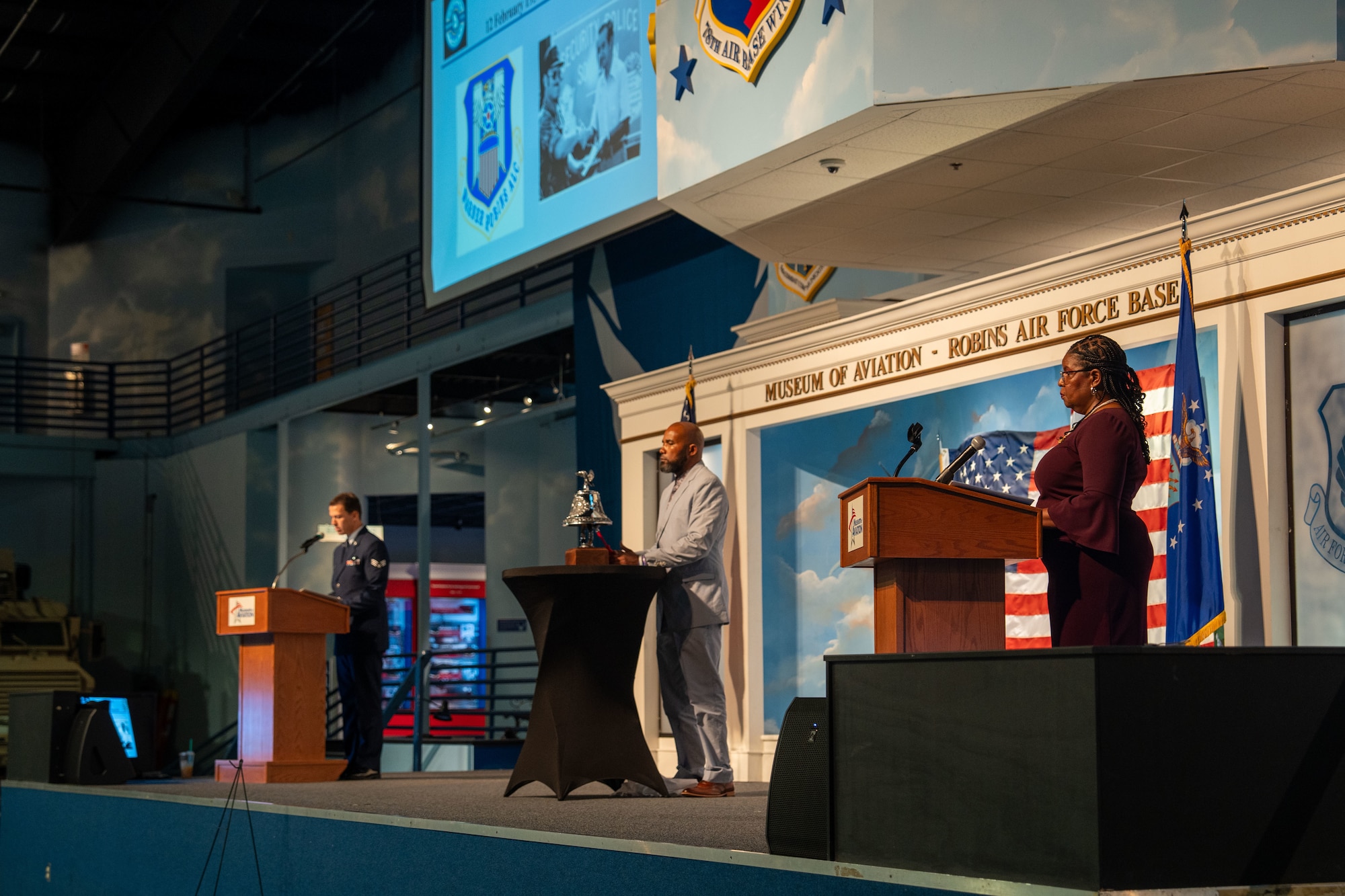 Three people standing on stage while person in middle rings a bell