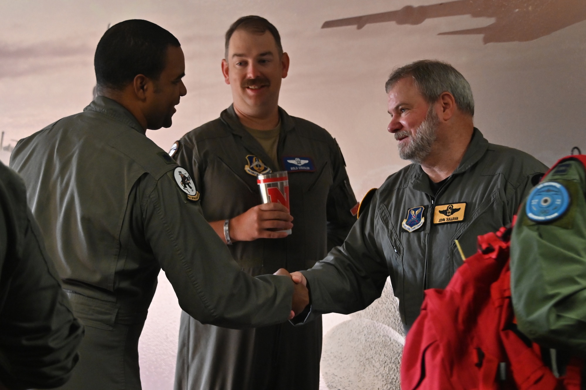 Two men shake hands while another looks on