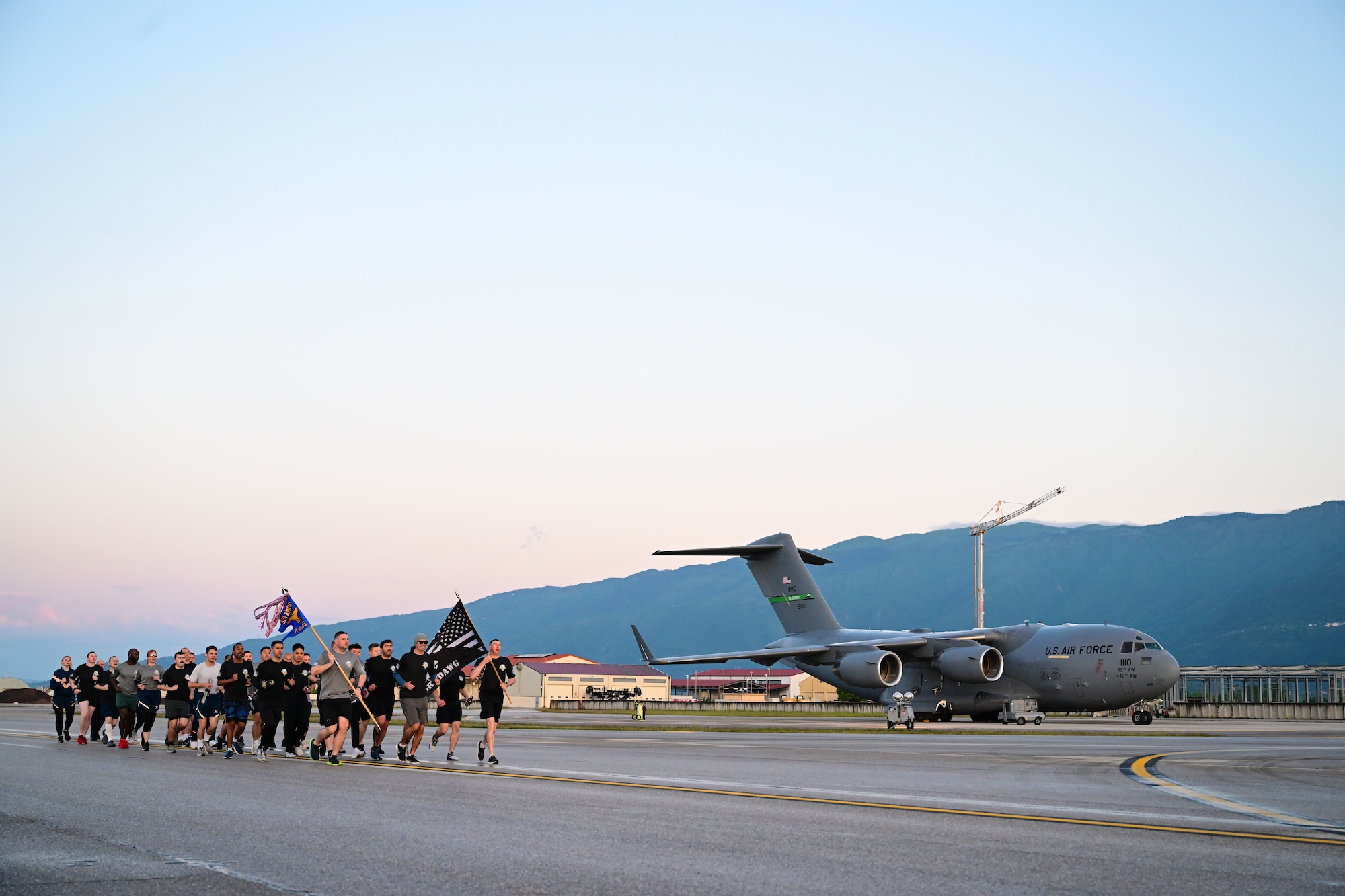 A formation runs down the flightline at sunrise passing a large plane