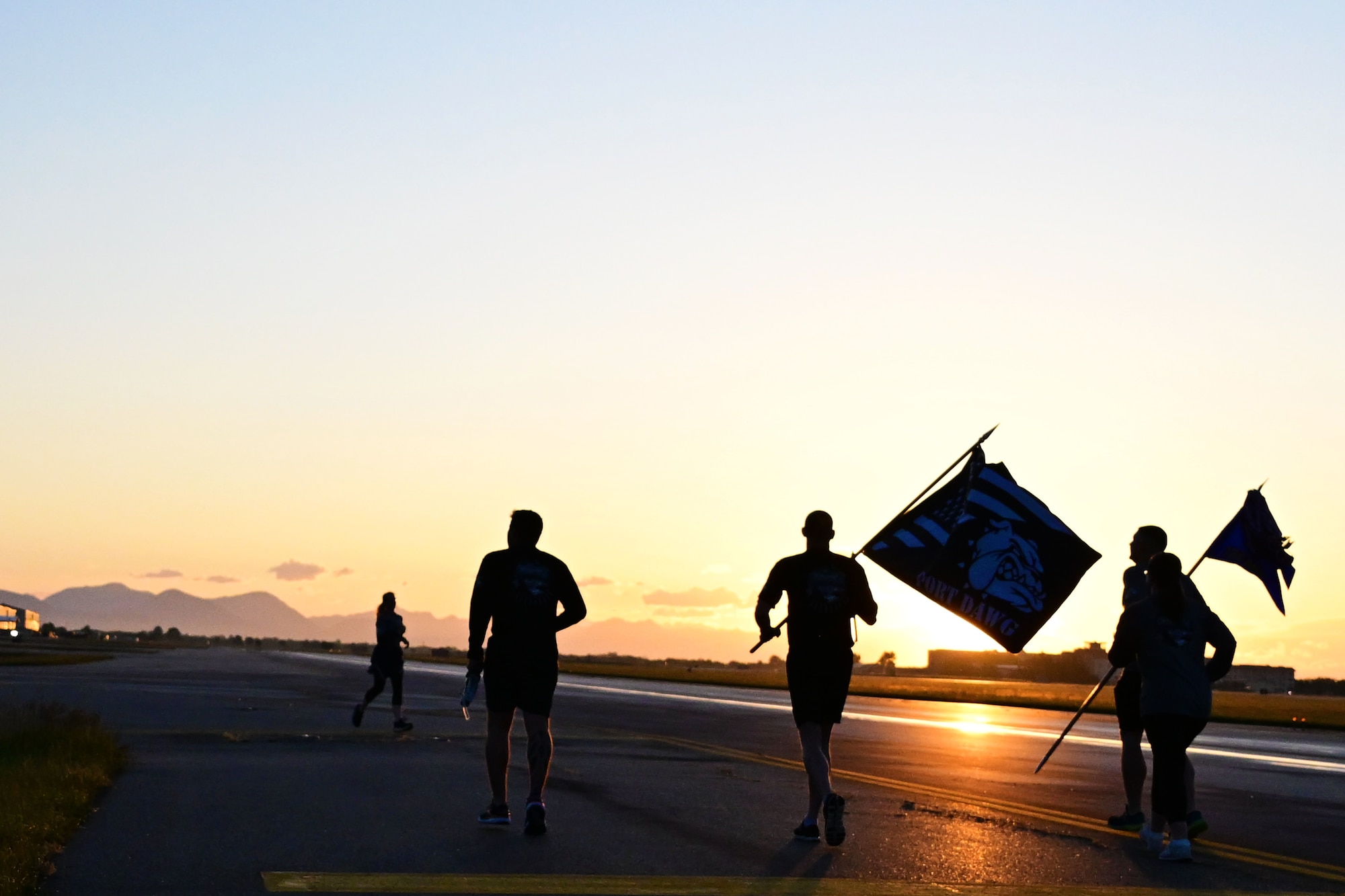 People run across the flightline at sunrise carrying a port dawg flag
