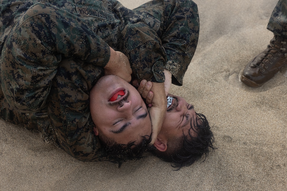 U.S. Marine Corps Cpl. Diego Perez, a finance technician, executes a choke hold on Lance Cpl. Marcos Albertorocha, a combat graphics specialist, both with Headquarters Battalion, Marine Corps Base Hawaii (MCBH), during physical training (PT) at Fort Hase Beach, MCBH, May 16, 2025. The PT included a grappling session in order to improve close-quarters combat skills as well as promote unit cohesion and encourage friendly competition between the Finance and Communication Strategy and Operations sections. (U.S. Marine Corps photo by Cpl. Jade K. Venegas)