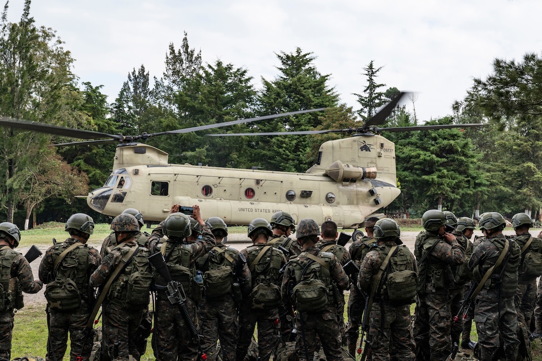 A group of Honduran and El Salvadorian soldiers look at a U.S. helicopter