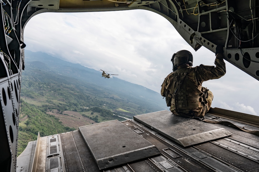 A U.S. service members sits on the back of a helicopter overlooking another helicopter in the distance