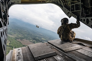 A U.S. service members sits on the back of a helicopter overlooking another helicopter in the distance