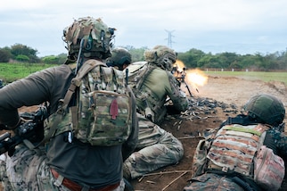 Guatemalan and U.S. service members crouch and lay on a berm while simulating cover fire during an exercise