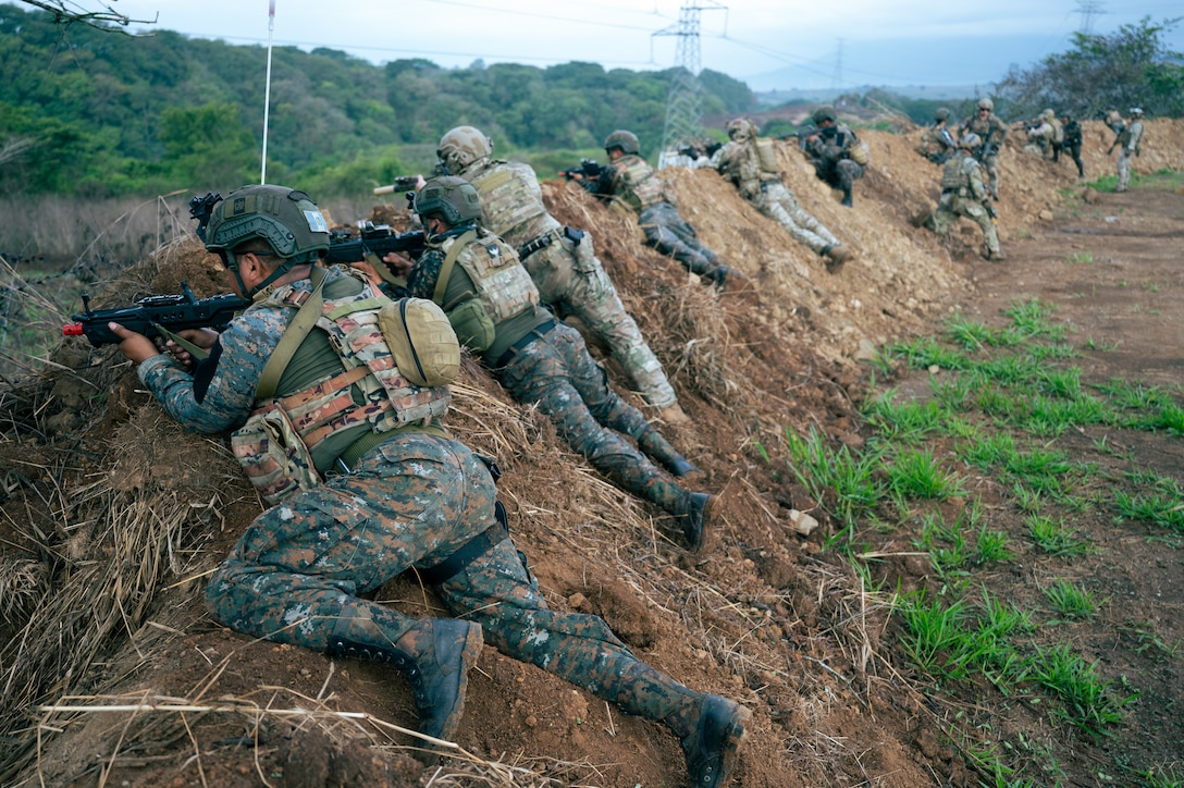 Guatemalan and U.S. service members lay on a man made berm while overlooking the surrounding area