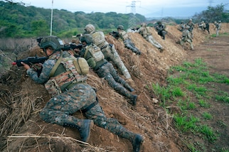 Guatemalan and U.S. service members lay on a man made berm while overlooking the surrounding area