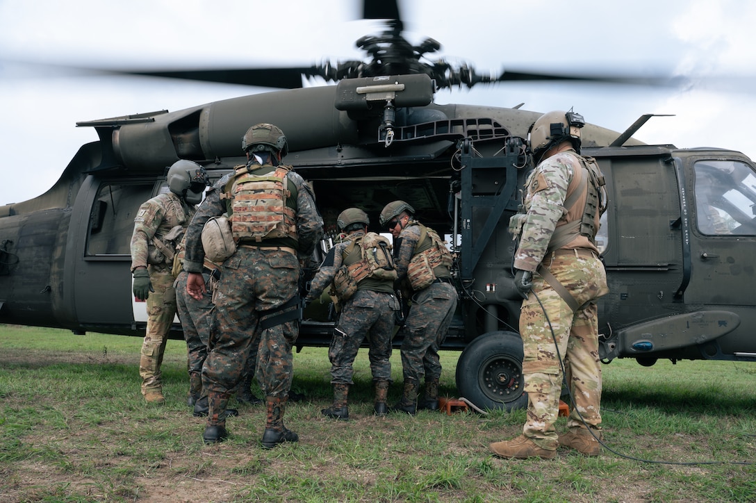 U.S. and Guatemalan service members stand in front of a U.S. helicopter