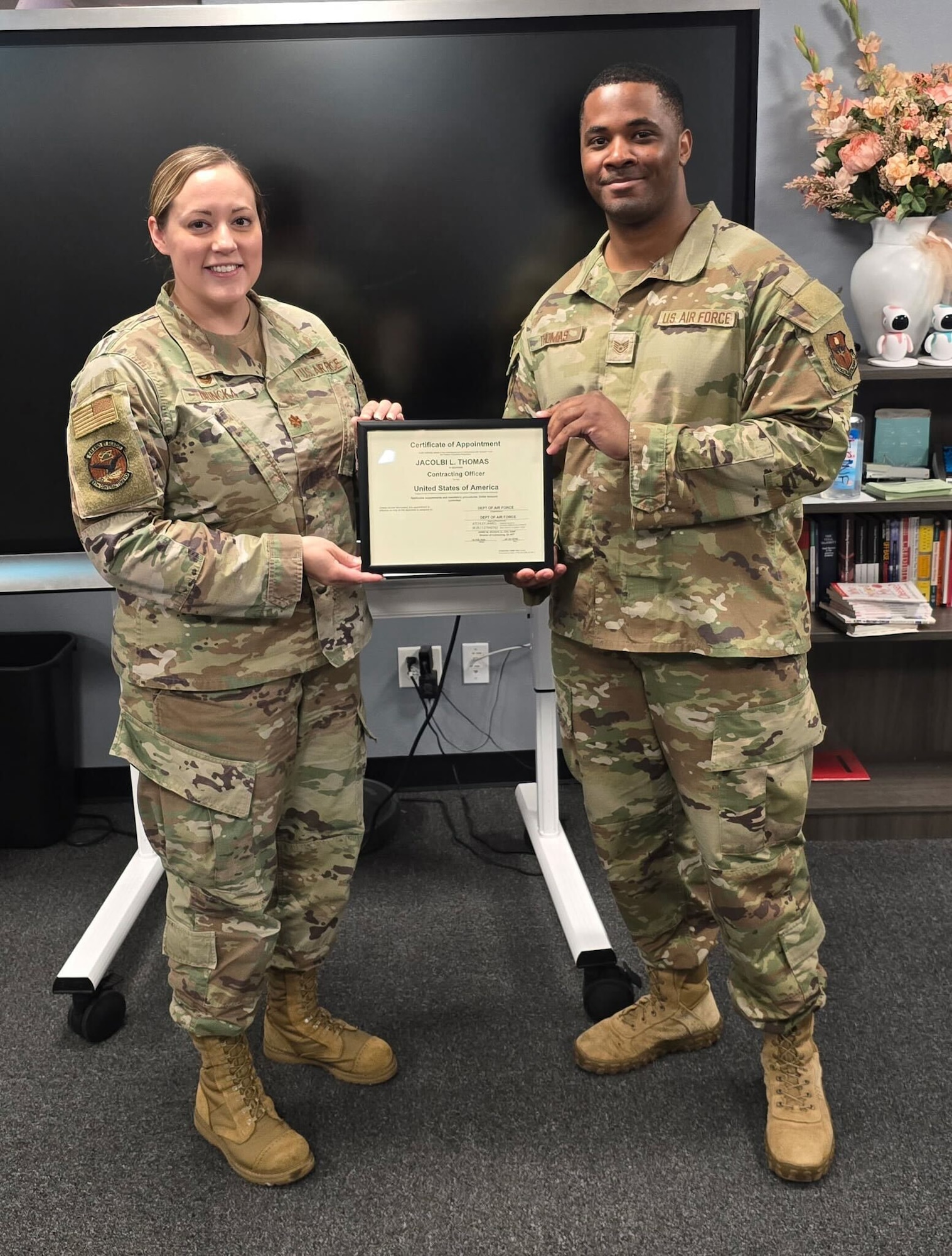 U.S. Air Force Maj. Chelsea Brincka, 97th Contracting Flight (CONF) commander and Staff Sgt. Jacolbi Thomas, 97th CONF infrastructure flight chief, poses with Thomas’ unlimited warrant certificate after a successful board interview at Altus Air Force Base, Oklahoma, May 1, 2025. This rare achievement highlights his expertise, leadership, and dedication to the contracting career field. (Courtesy photo from Lori Clinton)