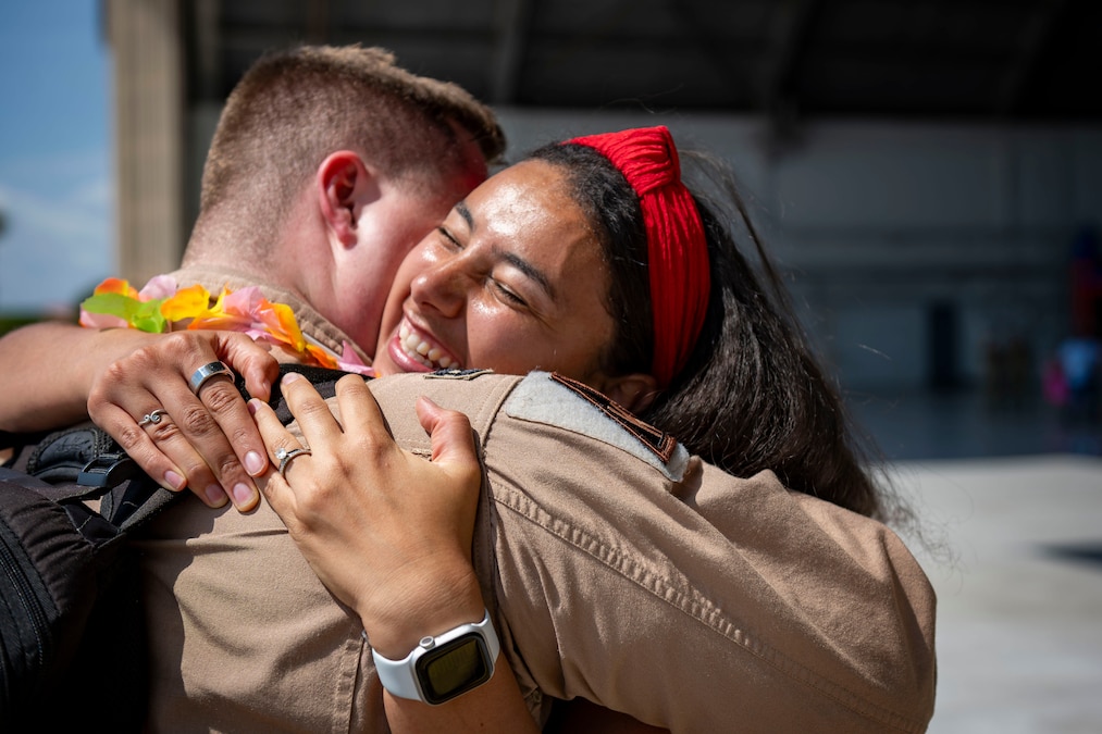 A smiling civilian hugs an airman on a flight line.
