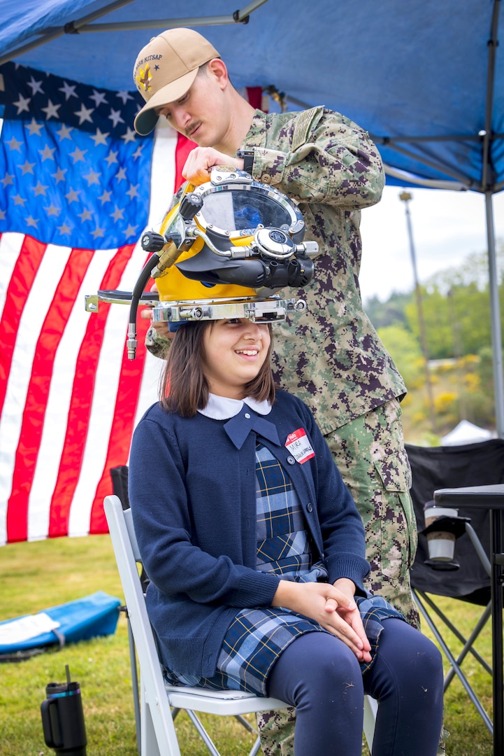 Navy Diver Petty Officer 3rd Class Gavin Hall, Bangor Dive Locker, helps students try on diving helmets May 14, 2025, during the 2025 Kitsap Water Festival at the Kitsap County Fairgrounds in Bremerton, Washington. (U.S. Navy photo by Wendy Hallmark)