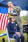 Navy Diver Petty Officer 3rd Class Gavin Hall, Bangor Dive Locker, helps students try on diving helmets May 14, 2025, during the 2025 Kitsap Water Festival at the Kitsap County Fairgrounds in Bremerton, Washington. (U.S. Navy photo by Wendy Hallmark)