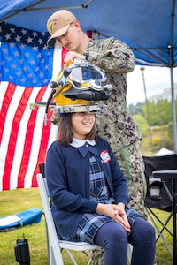 Navy Diver Petty Officer 3rd Class Gavin Hall, Bangor Dive Locker, helps students try on diving helmets May 14, 2025, during the 2025 Kitsap Water Festival at the Kitsap County Fairgrounds in Bremerton, Washington. (U.S. Navy photo by Wendy Hallmark)