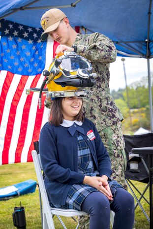 Navy Diver Petty Officer 3rd Class Gavin Hall, Bangor Dive Locker, helps students try on diving helmets May 14, 2025, during the 2025 Kitsap Water Festival at the Kitsap County Fairgrounds in Bremerton, Washington. (U.S. Navy photo by Wendy Hallmark)