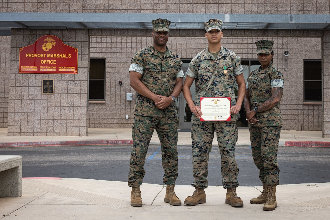 U.S. Marine Corps Brig. Gen. Nick Brown and Sgt. Maj. Sherri Cook, the commanding general and senior enlisted leader of Marine Corps Installations West, Marine Corps Base Camp Pendleton, pose for a photo with Lance Cpl. Marcus Benson, a military police augment with Provost Marshal Office, MCIW, MCB Camp Pendleton, center, on MCB Camp Pendleton, Calif., April 15, 2025. Benson, a Texas native, received an award for ending an active police pursuit on March 3, 2025. (U.S. Marine Corps photo by Cpl. Jacqueline Akamelu)