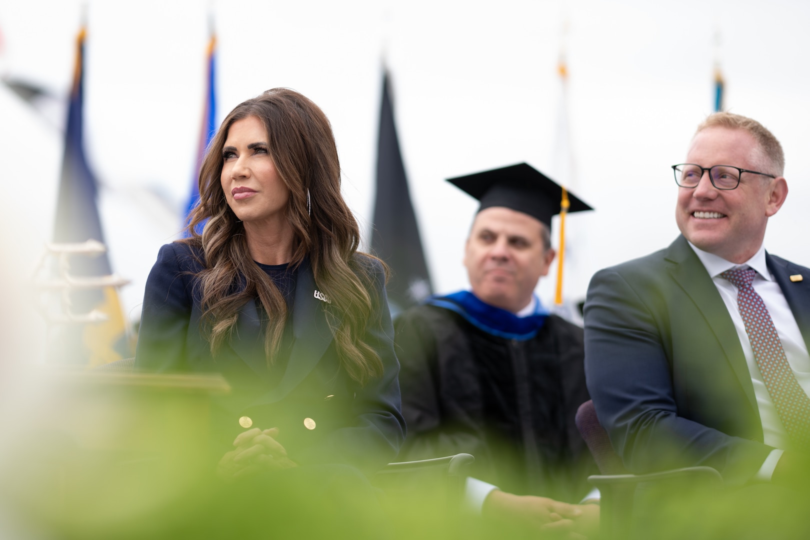 U.S. Secretary of Homeland Security Kristi Noem (left) and Senior Advisor to the Secretary for the U.S. Coast Guard Sean Plankey (right) listen during a speech at the 144th Commencement Exercises. Noem shared the details of Force Design 2028, which includes plans to purchase new aircraft, grow the workforce by 15,000 personnel, fix aging facilities, and begin a once-in-a-generation transformation of the 234-year old maritime service. (U.S. Coast Guard photo by Petty Officer Second Class Janessa Warschkow.)