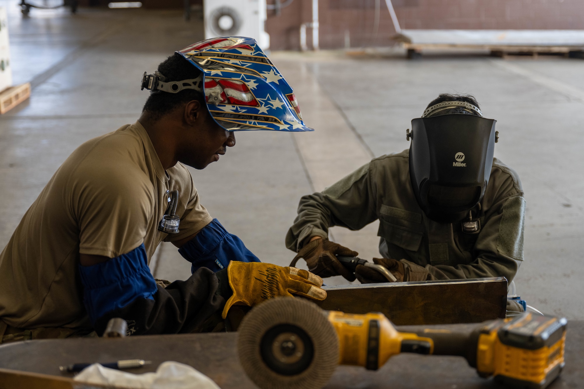 Two U.S. Air Force Airmen look over a piece of metal before performing a welding task in their shop.