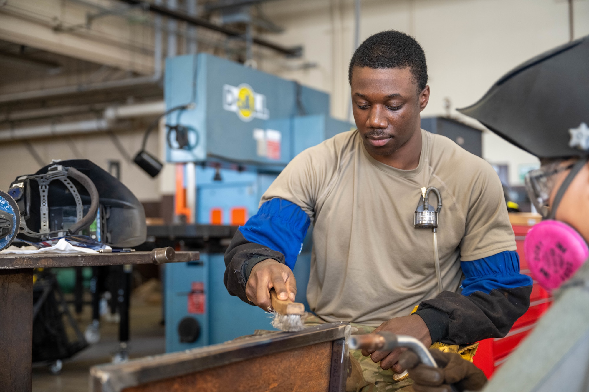 A U.S. Air Force Airmen brushes a freshly welded piece of metal as part of an aircraft part.