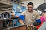 A U.S. Air Force Airmen brushes a freshly welded piece of metal as part of an aircraft part.