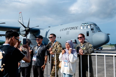 U.S. Air Force Master Sgt. Chaz Burrows, 374th Aircraft Maintenance Squadron programs flight chief, and Tech. Sgt. Kaylynn Staba, 36th Airlift Squadron instructor loadmaster, pose for a photo with attendees at the Langkawi International Maritime and Aerospace Exhibition 2025 in Langkawi, Malaysia, May 20, 2025. The 36 Airlift Squadron maintains mission-ready C-130J aircrew to conduct a wide variety of mission sets; including theater airlift, special operations, and humanitarian aid throughout the Indo-Pacific. (U.S. Air Force photo by Senior Airman Alexzandra Gracey)