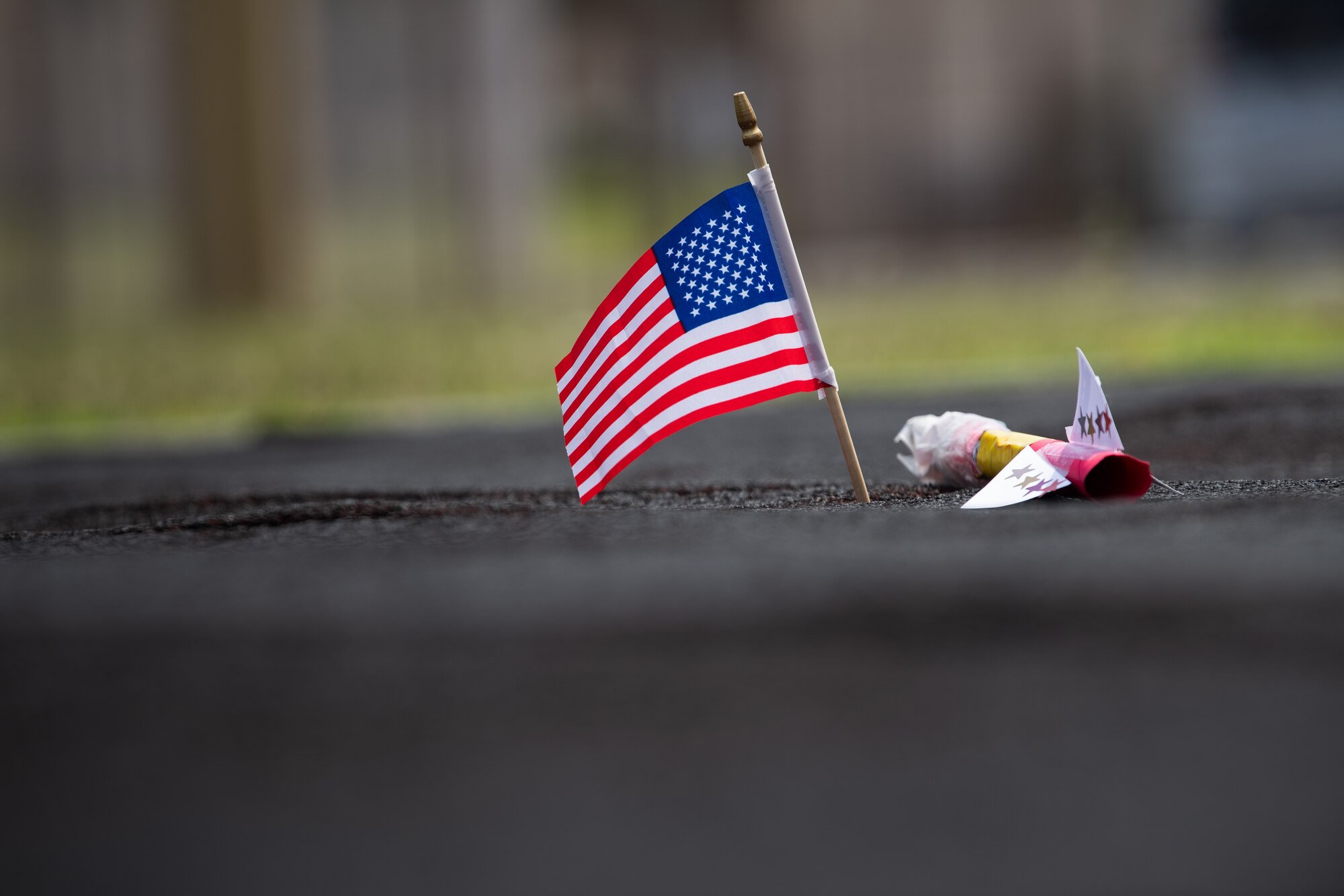 A small American flag sits in the ground beside a model rocket.