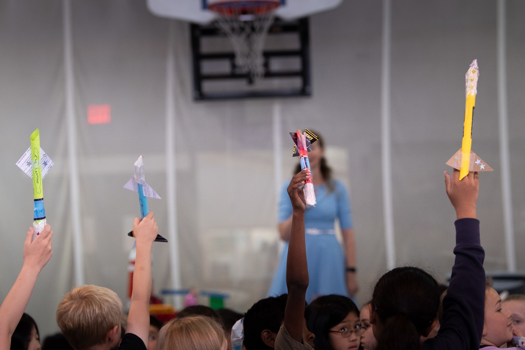 Students hold their model rockets that are each of different colors in the air during a presentation about the U.S. Space Force.