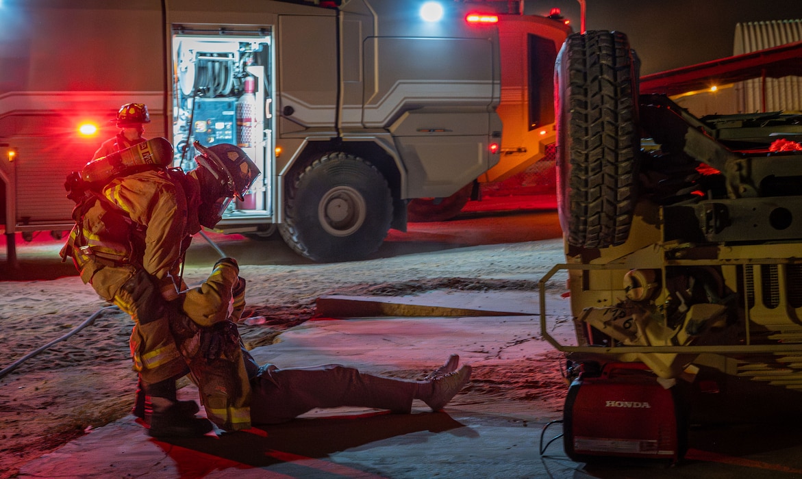 A firefighter pulls a person away from a flipped Humvee.