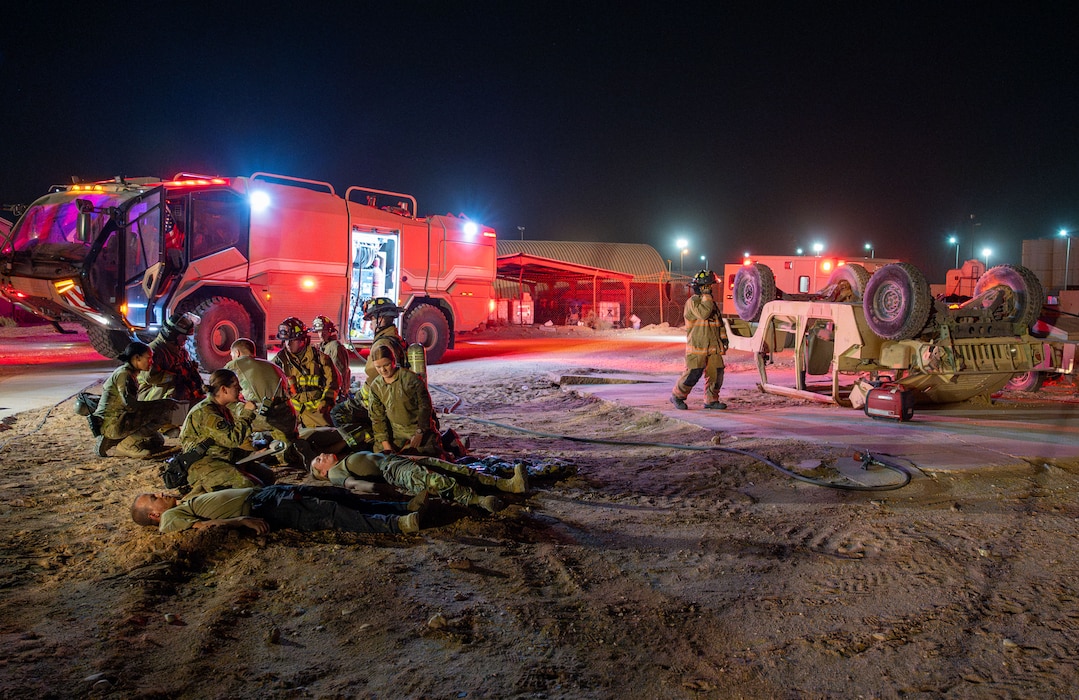 A wide shot of the exercise scene is shown with firetrucks, a rolled Humvee, and first responders treating simulated casualties.