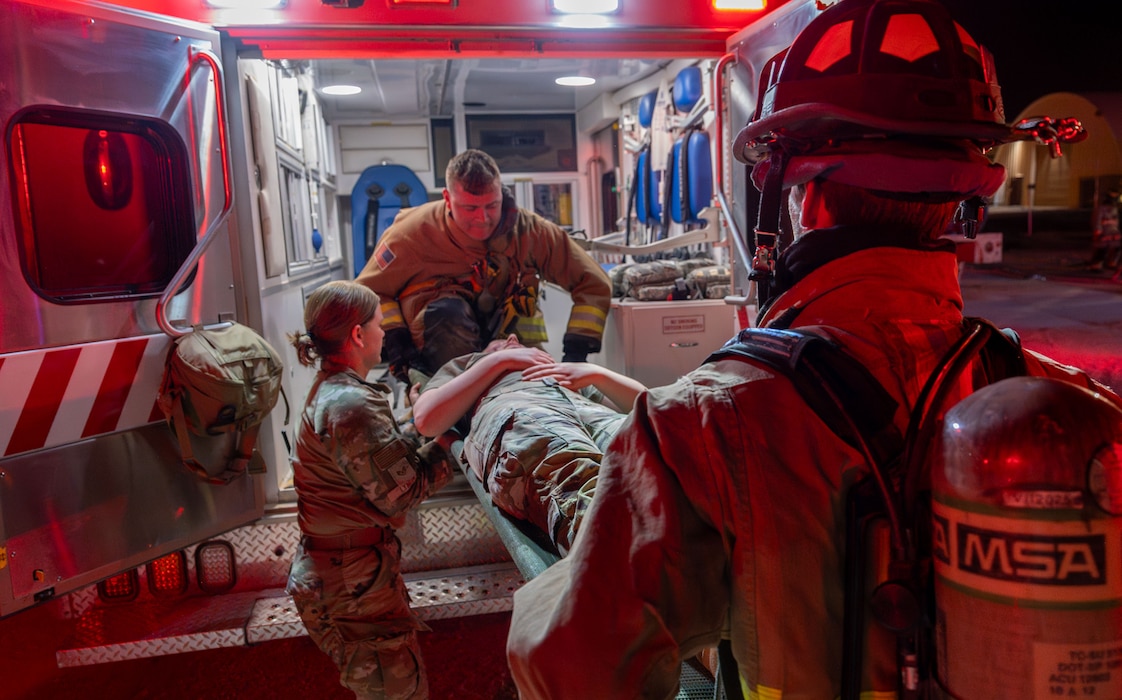 Airmen load a person on a gurney into the back of an ambulance.