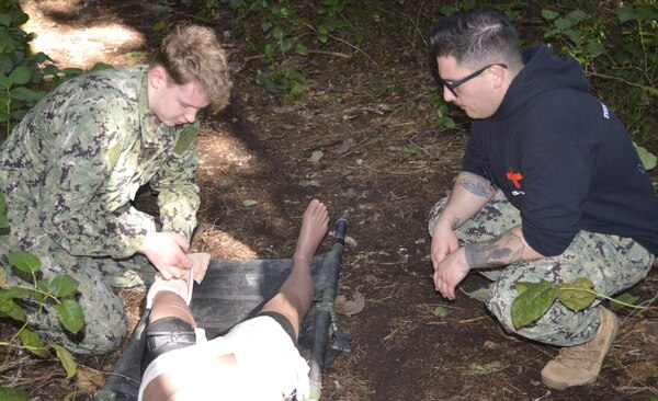 Field of battle scrutiny…under the watchful – and demanding – gaze of Hospital Corpsman 1st Class (Fleet Marine Force qualified) Austin Santistevan, Navy Medicine Readiness Training Command Bremerton Tactical Combat Casualty Care course instructor, Hospitalman Joseph Clark is actively critiqued on his response ability to a battlefield injury. TCCC is an operational necessity for Clark and all other corpsmen and is specifically designed to simulate the unique challenges and conditions on the field of battle in handling traumatic injuries. For Santistevan, teaching the Tactical Combat Casualty Care course is a labor of love. “I love being a TCCC instructor. I can teach a course and know I’m making a difference,” said Santistevan, a 13-year Navy veteran, from Pueblo, Colorado and a Centennial High School grad, “home of the Bulldogs.” (official Navy photo by Douglas H Stutz, NHB/NMRTC Bremerton public affairs officer).