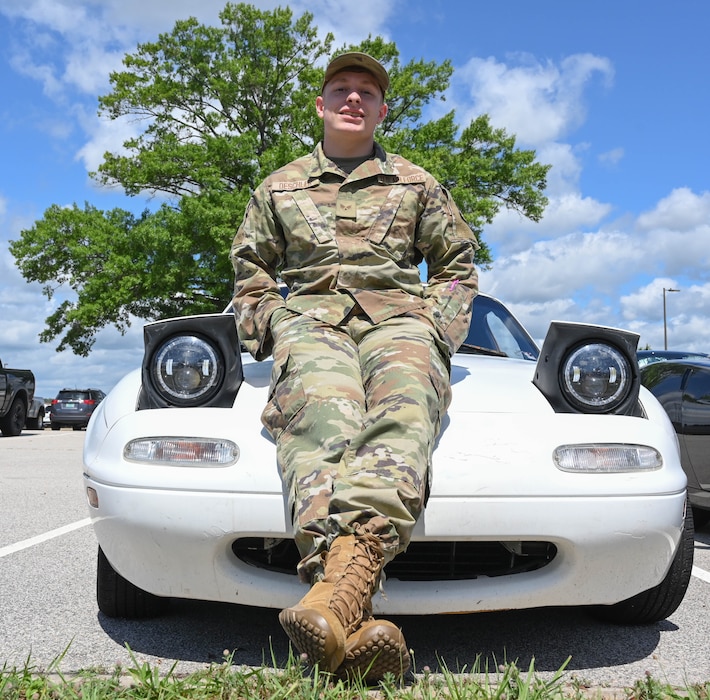 An Airman sits on the hood of a car.