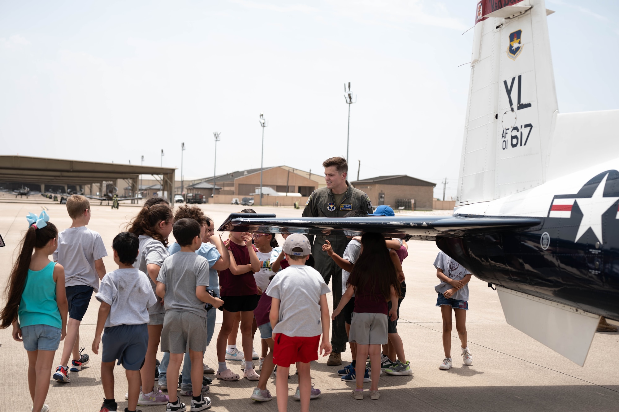 Students gather under the wing of a T-6 Texan II alongside U.S. Air Force Capt. Noah Collins, 85th Flying Training Squadron instructor pilot, during a Ceniza Hills School tour at Laughlin Air Force Base, Texas, May 15, 2025. The tour aimed to educate and inspire future generations about Air Force aviation. (U.S. Air Force photo by Senior Airman Keira Rossman)