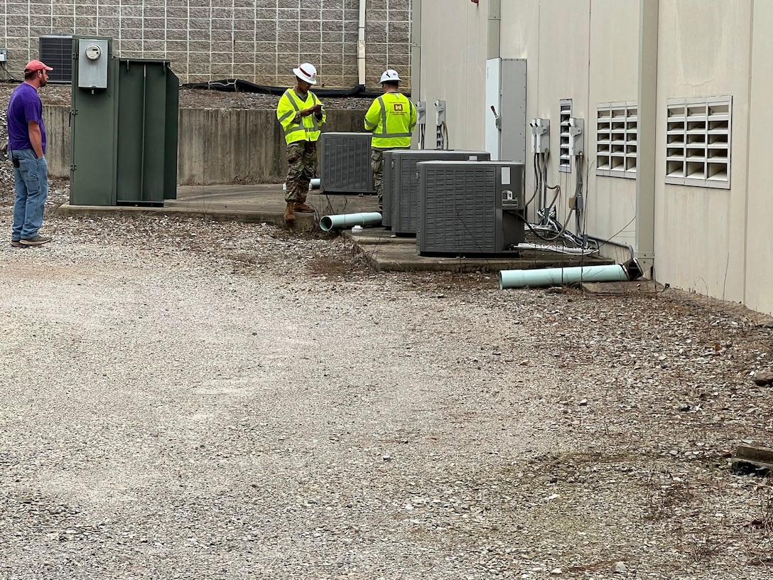 Two soldiers stand near air conditioning units as they determine their size and power needs.