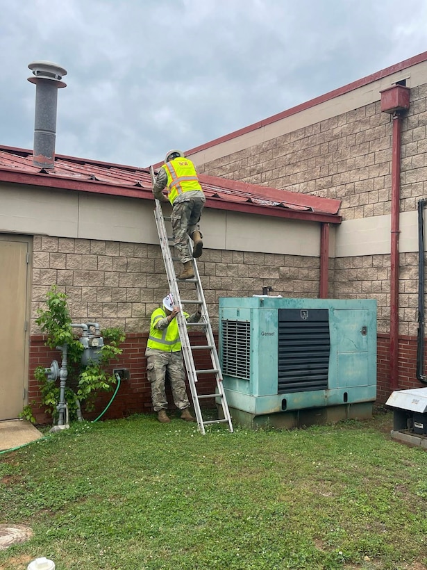 A soldier climbs a ladder to get on top of a roof while another holds on to the bottom to secure it.