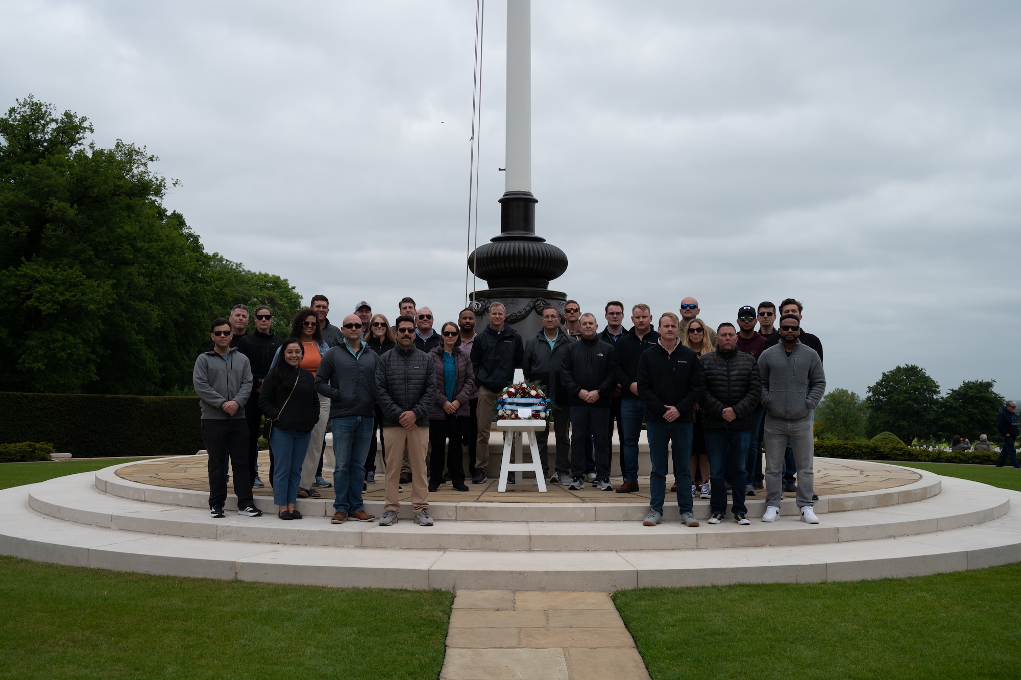 Individuals surrounding a wreath in front of a flagpole