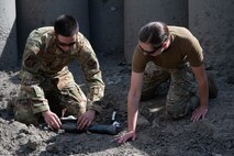 Senior Airman Arthur Pancoast, 5th Civil Engineer Squadron Explosive Ordnance Disposal journeyman, (left), and Capt. Natalie Petro, Explosive Ordnance Disposal flight commander, (right), attach a detonating cord to a shape charge at Minot Air Force Base, North Dakota, May 12, 2025. A detonating cord was used in this training exercise to properly control the detonation of the shape charge remotely. (U.S. Air Force photo by Airman 1st Class Wesley Davies)