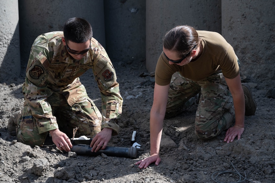Senior Airman Arthur Pancoast, 5th Civil Engineer Squadron Explosive Ordnance Disposal journeyman, (left), and Capt. Natalie Petro, Explosive Ordnance Disposal flight commander, (right), attach a detonating cord to a shape charge at Minot Air Force Base, North Dakota, May 12, 2025. A detonating cord was used in this training exercise to properly control the detonation of the shape charge remotely. (U.S. Air Force photo by Airman 1st Class Wesley Davies)