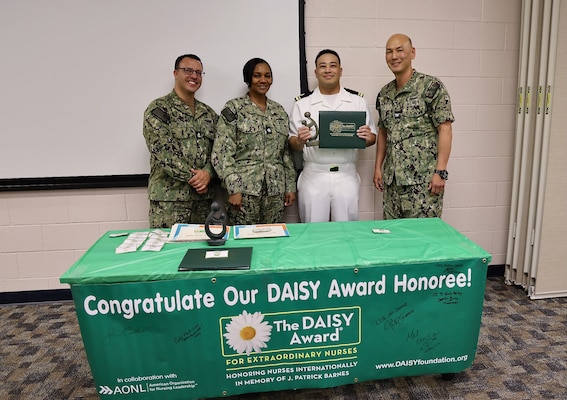 Lt. j.g. Aaron Gracad (center-right), a San Diego, Calif. native working in the Maternal Infant Nursing Department is honored during the 2025 DAISY Award ceremony held at Naval Hospital Twentynine Palms on May 16. The DAISY Award recognizes outstanding nursing professionals who demonstrate exceptional compassion and dedication to patient-centered care. The event also highlighted nominees from multiple hospital departments, showcasing the wide-reaching commitment to quality healthcare across the facility (U.S. Navy photo by Christopher C. Jones, NHTP/NMRTC Twentynine Palms public affairs officer).