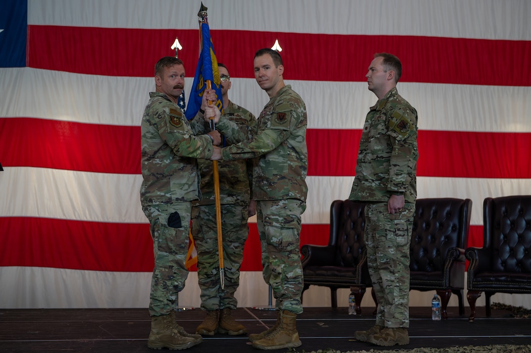 A man hands over a guidon to another man as people watch on.