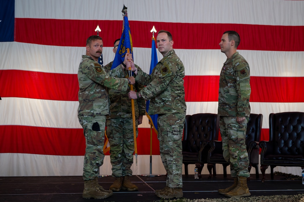A man hands over a guidon to another man as people watch on.
