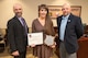 Three people pose for a photo, the person standing in the middle is holding two awards.
