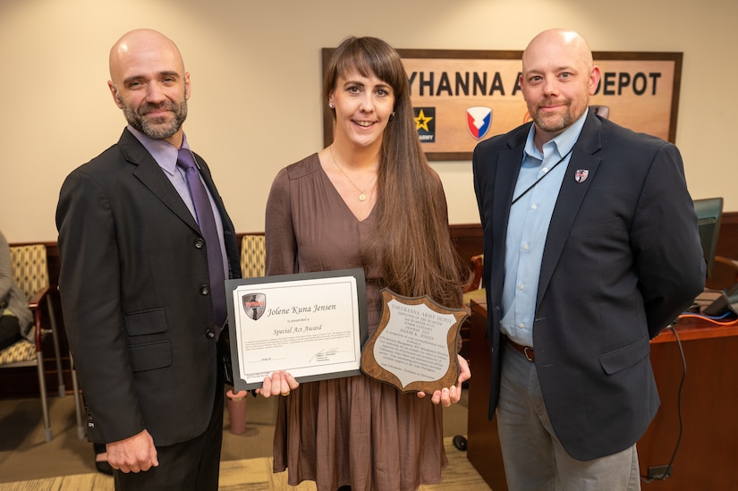 Three people pose for a photo, the person standing in the middle is holding two awards.