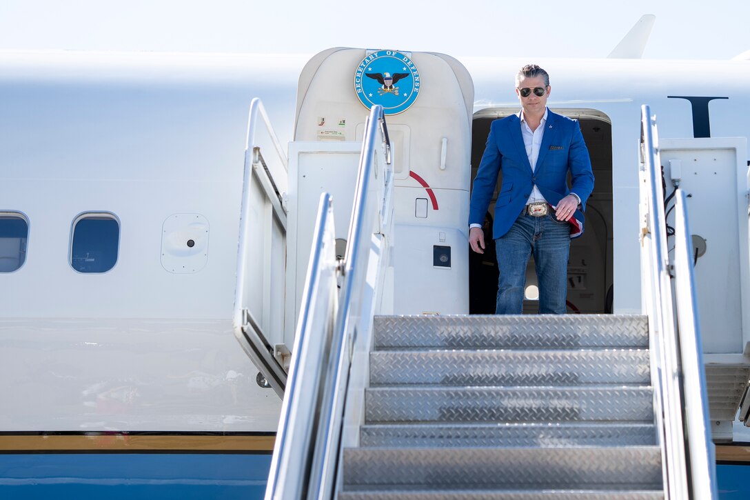 A man wearing a suit exits a white airplane with blue accents.