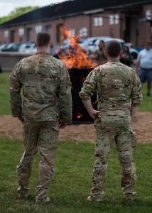 Two Airmen stand in front of a burning piano outdoors