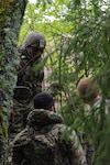 U.S. Army Spc. Olu Achu, a forward observer (left), Spc. Derrick Hyman, a radio telephone operator, Sgt. Kyle Troyer, a forward observer, with 1st Battalion, 107th Field Artillery, Detachment 1, Maryland Army National Guard, move through the woods while awaiting air support during Exercise Hedgehog near Võru, Estonia, May 14, 2025.