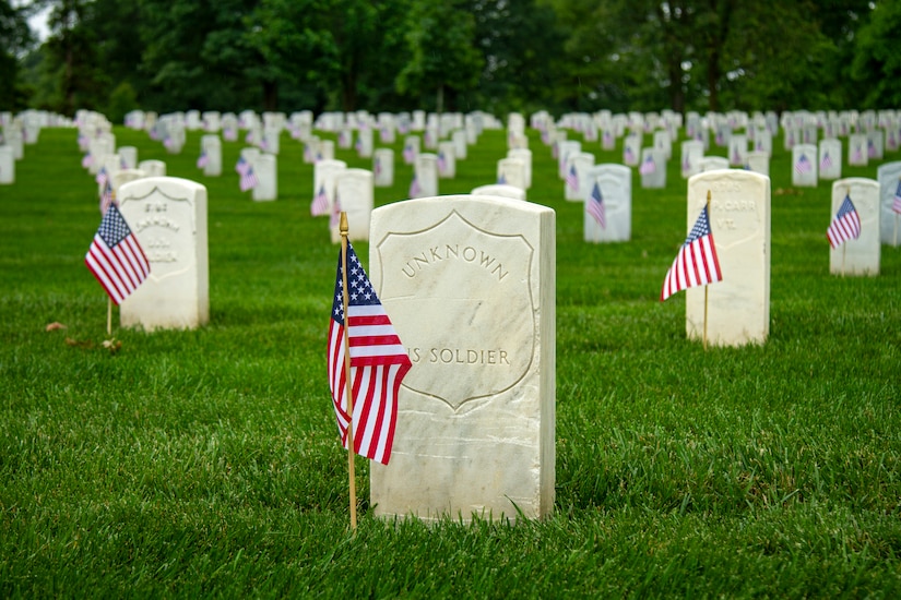 Small U.S. flags stand in front of white tomb stones at a gravesite.