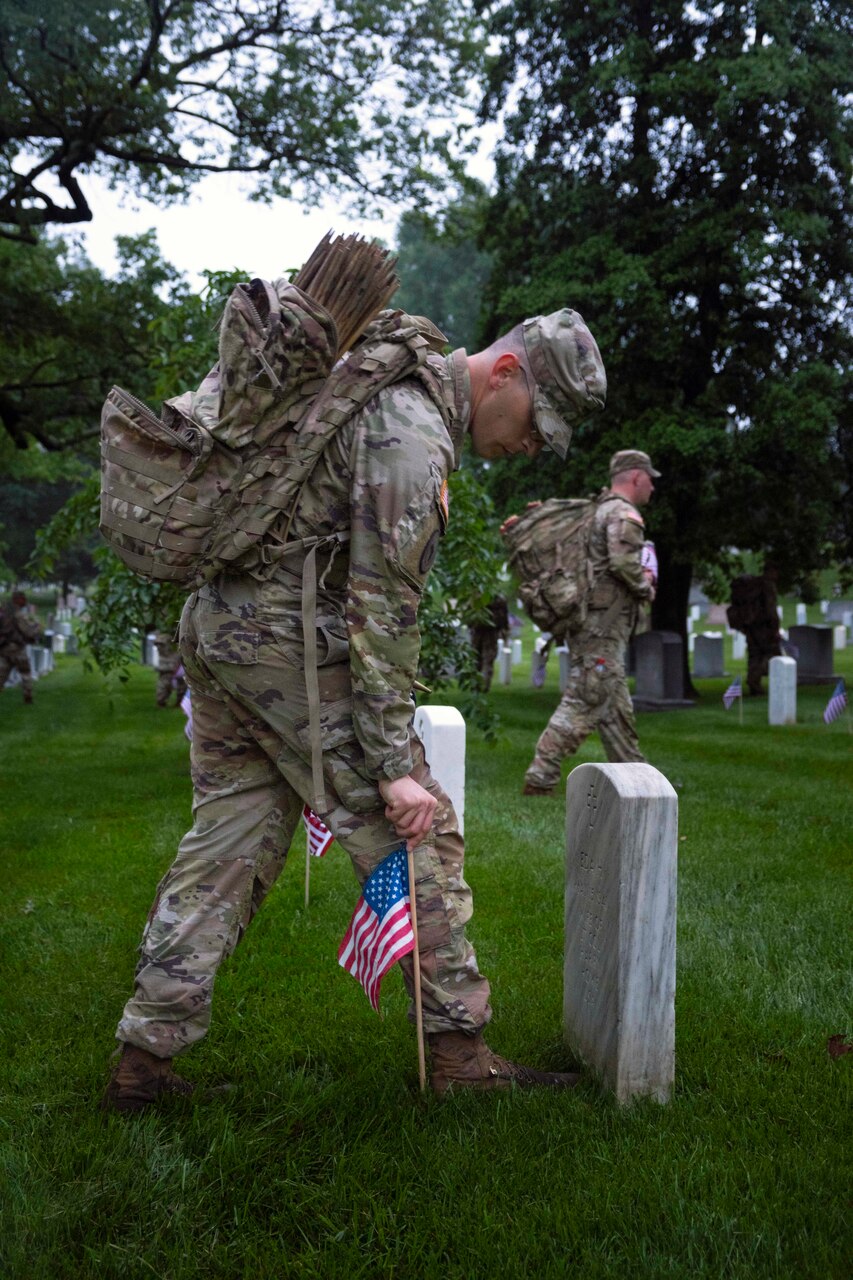 A soldier places a U.S. flag at a gravesite during an overcast day.