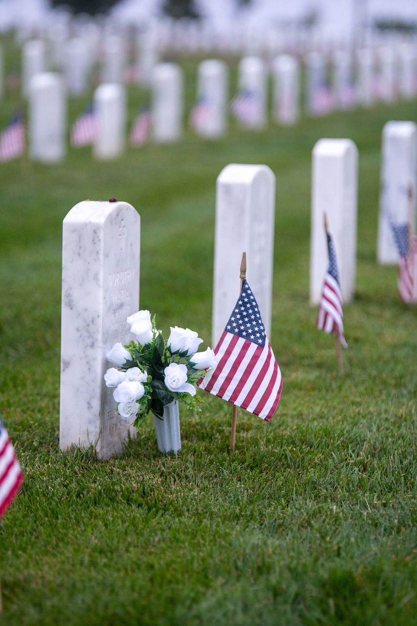 A bouquet of flowers sits beside a U.S. flag in front of a marble gravesite.