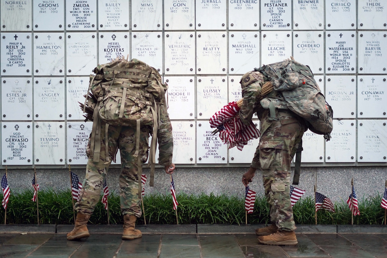 Two soldiers place U.S. flags at columbarium niches during an overcast day.