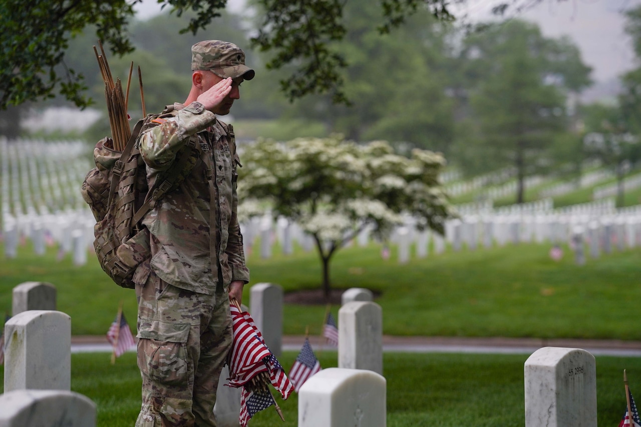A soldier salutes at a gravesite during an overcast day.
